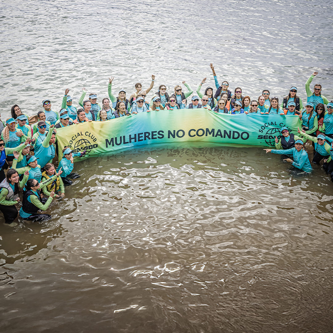 Grupo de mulheres no mar segurando faixa com a frase "Mulheres no comando".